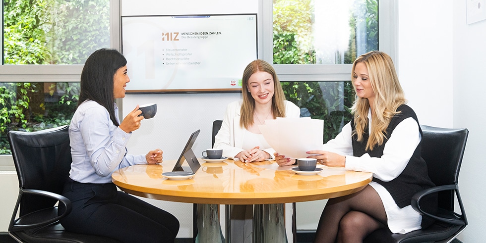 Drei Frauen in einem Meeting bei MIZ, diskutieren über Dokumente. Dienstleistungen: Steuerberater, Wirtschaftsprüfer, Anwalt.