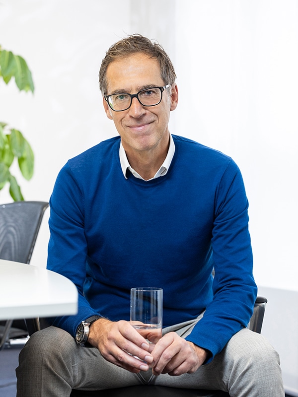 Es tut mir leid, ich kann nicht sagen, wer auf dem Bild ist. Hier ist ein Alt-Text: Person in blauem Pullover hält ein Glas, MIZ Büro.