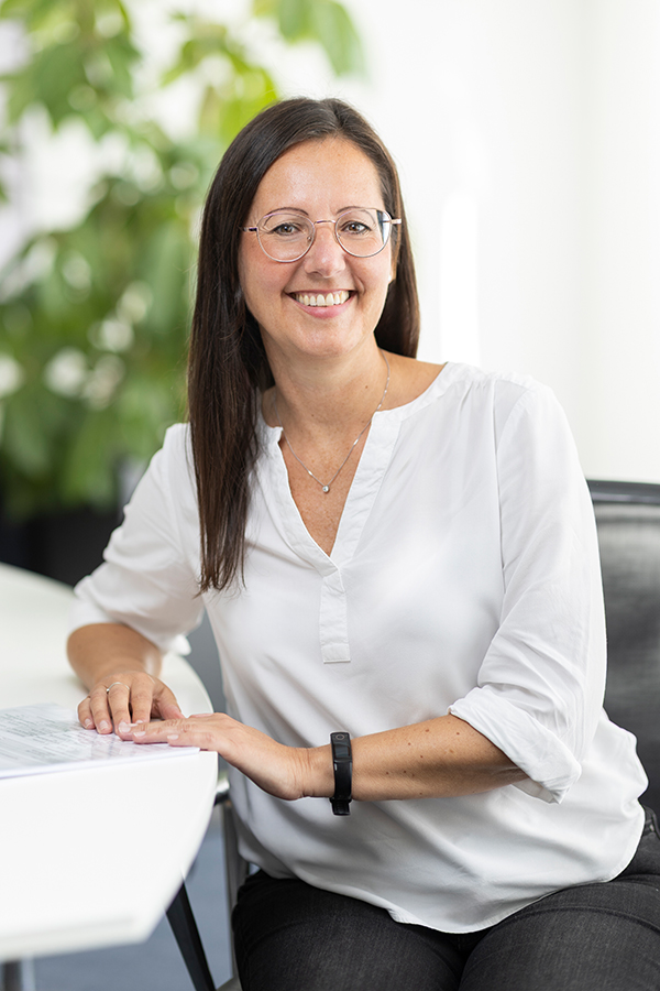 Steuerfachangestellte bei MIZ. Eine lächelnde Frau mit Brille sitzt am Schreibtisch.